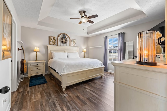 bedroom featuring ceiling fan, dark wood-type flooring, a textured ceiling, and a raised ceiling