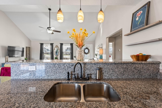 kitchen featuring sink, decorative light fixtures, dark stone counters, and vaulted ceiling