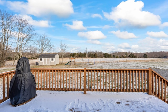 snow covered deck featuring a rural view, a playground, and a shed