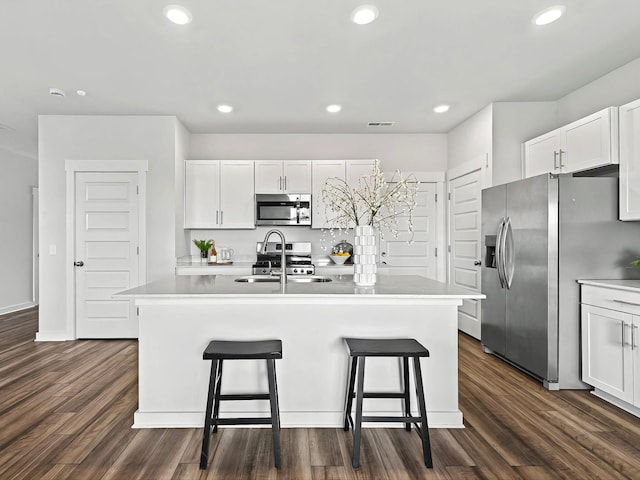 kitchen featuring stainless steel appliances, dark hardwood / wood-style floors, a center island with sink, and white cabinets