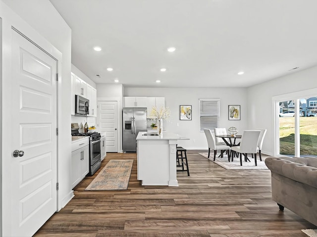 kitchen with stainless steel appliances, white cabinetry, a kitchen island with sink, and a kitchen bar