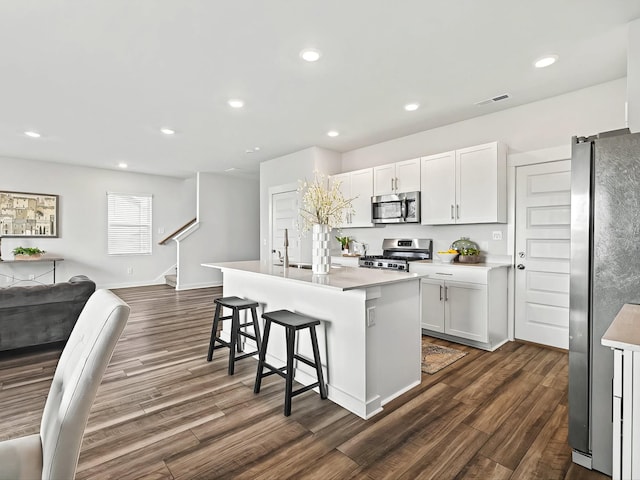 kitchen with white cabinetry, appliances with stainless steel finishes, a kitchen island with sink, and dark hardwood / wood-style flooring