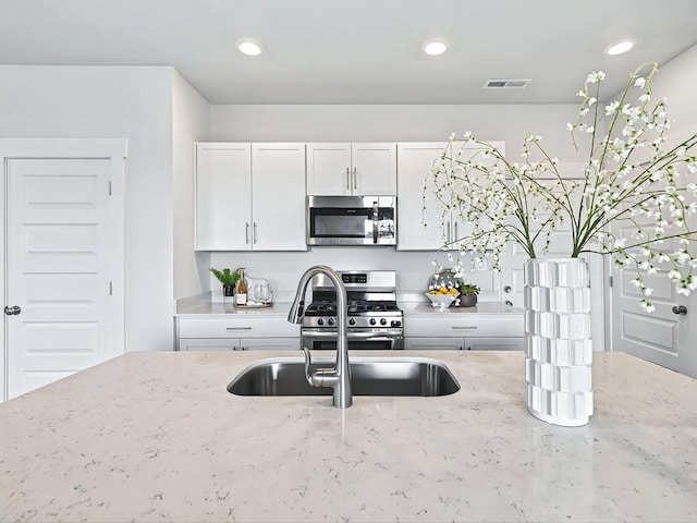 kitchen with stainless steel appliances, light stone countertops, sink, and white cabinets