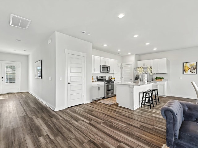 kitchen featuring stainless steel appliances, a breakfast bar, a kitchen island with sink, and white cabinets