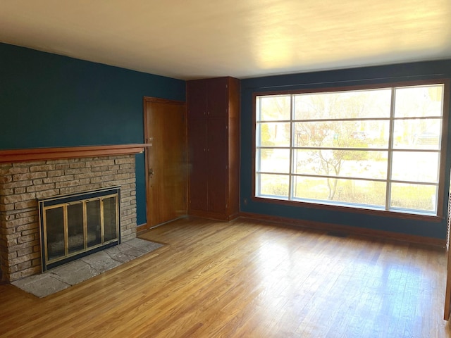 unfurnished living room featuring a brick fireplace, light hardwood / wood-style flooring, and plenty of natural light