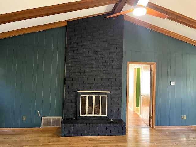 unfurnished living room featuring lofted ceiling with beams, a brick fireplace, and hardwood / wood-style flooring