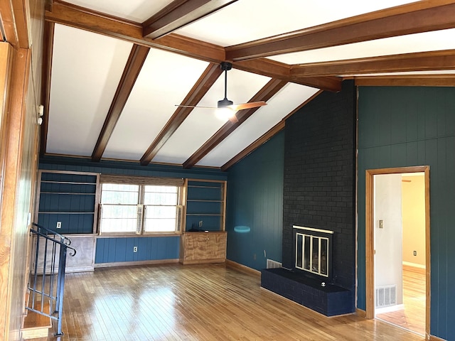 unfurnished living room with hardwood / wood-style flooring, a brick fireplace, lofted ceiling with beams, and ceiling fan