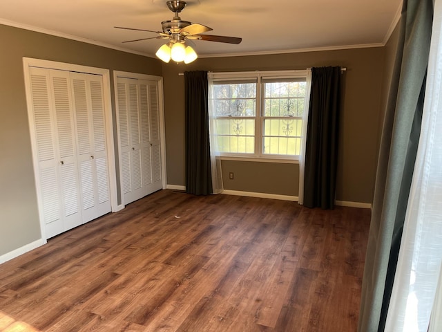 unfurnished bedroom with ceiling fan, multiple closets, dark wood-type flooring, and ornamental molding