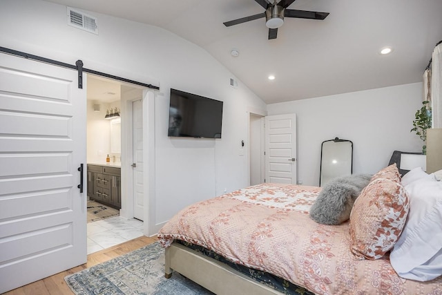 bedroom featuring lofted ceiling, ensuite bath, light wood-type flooring, ceiling fan, and a barn door