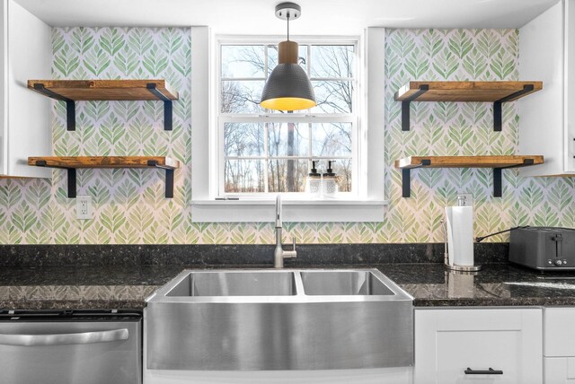 kitchen with white cabinetry, hanging light fixtures, dark stone counters, stainless steel dishwasher, and sink