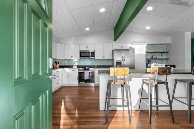 kitchen with white cabinetry, dark hardwood / wood-style flooring, stainless steel appliances, tasteful backsplash, and a breakfast bar area