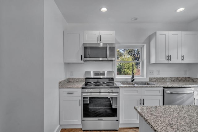 kitchen featuring sink, light stone counters, stainless steel appliances, and white cabinetry