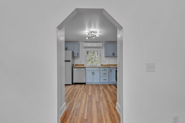 kitchen featuring appliances with stainless steel finishes, wooden counters, light hardwood / wood-style floors, sink, and a wall mounted air conditioner