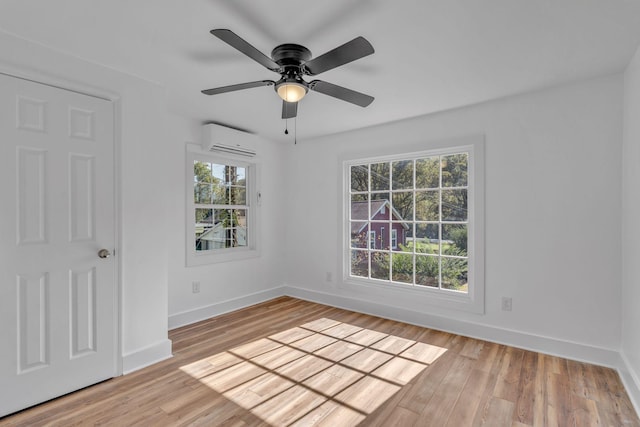 spare room with light hardwood / wood-style floors, plenty of natural light, a wall unit AC, and ceiling fan