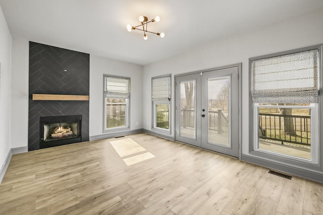 unfurnished living room with french doors, a large fireplace, and light hardwood / wood-style flooring