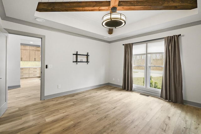 spare room with a raised ceiling and light wood-type flooring