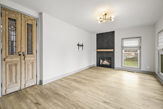 unfurnished living room with light hardwood / wood-style flooring, a large fireplace, and a chandelier