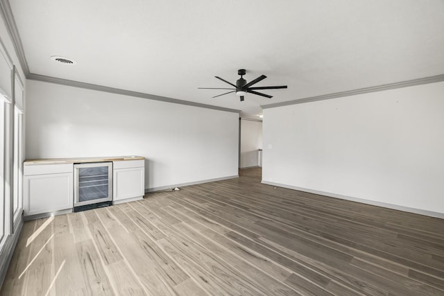 unfurnished living room with crown molding, ceiling fan, wine cooler, wood-type flooring, and bar area