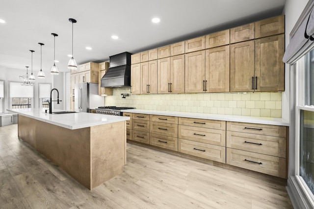 kitchen with sink, stainless steel refrigerator, a kitchen island with sink, custom range hood, and decorative backsplash