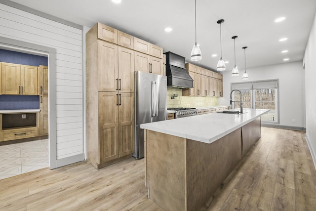 kitchen with sink, stainless steel refrigerator, hanging light fixtures, an island with sink, and custom range hood