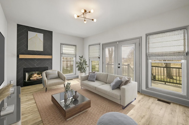 living room featuring french doors, a large fireplace, and light wood-type flooring