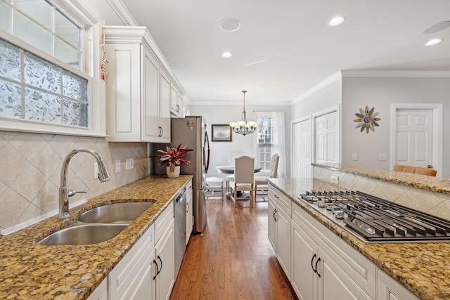 kitchen with sink, white cabinetry, hanging light fixtures, ornamental molding, and stainless steel appliances