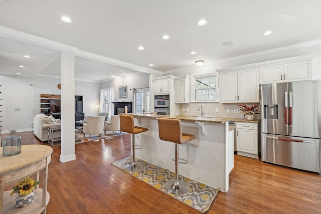 kitchen featuring white cabinets, a kitchen island, stainless steel appliances, a kitchen breakfast bar, and light stone counters