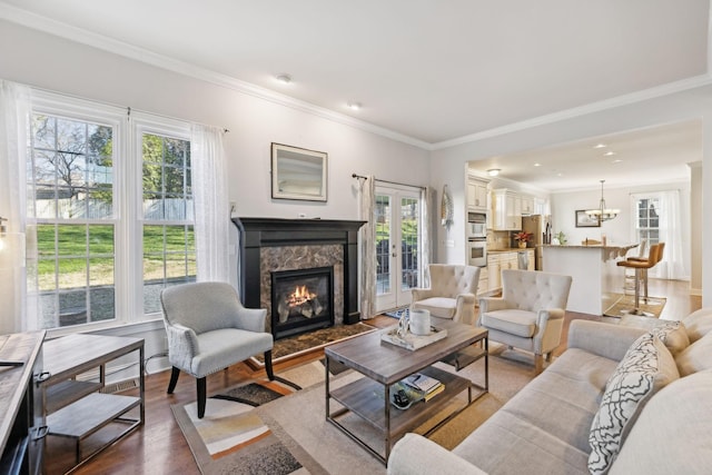 living room featuring an inviting chandelier, light hardwood / wood-style floors, ornamental molding, french doors, and a high end fireplace