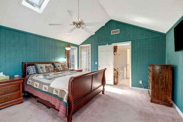 bedroom featuring light carpet, ceiling fan, vaulted ceiling with skylight, and connected bathroom