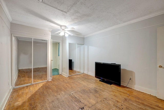 unfurnished bedroom with a textured ceiling, ceiling fan, hardwood / wood-style flooring, and multiple closets