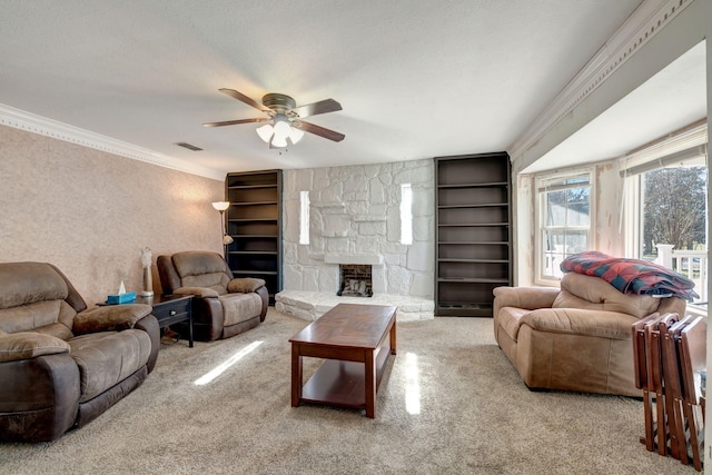 living room with ceiling fan, light colored carpet, a stone fireplace, ornamental molding, and built in shelves