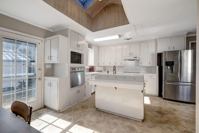 kitchen featuring a kitchen island with sink, a skylight, stainless steel appliances, ornamental molding, and white cabinets