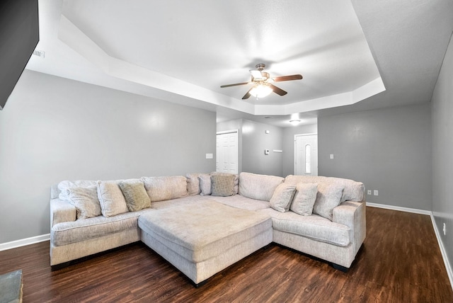 living room featuring ceiling fan, a tray ceiling, and dark hardwood / wood-style flooring