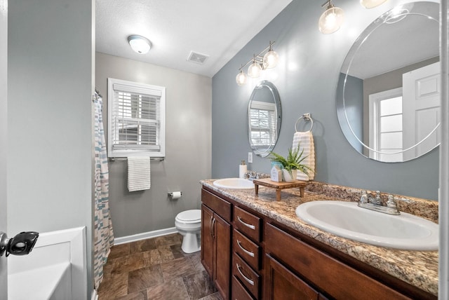 bathroom with a wealth of natural light, toilet, vanity, and a textured ceiling