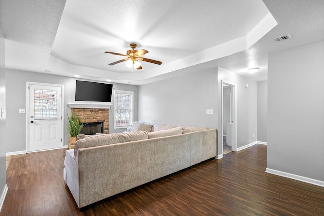 living room with plenty of natural light, a tray ceiling, dark hardwood / wood-style floors, and a fireplace