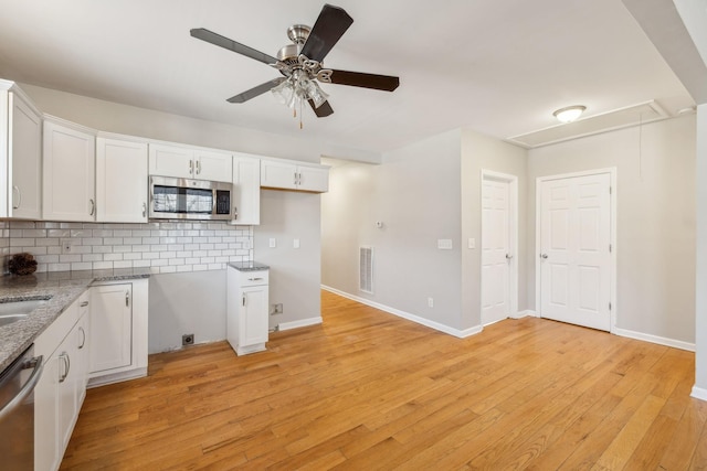 kitchen with white cabinets, backsplash, appliances with stainless steel finishes, and light hardwood / wood-style flooring