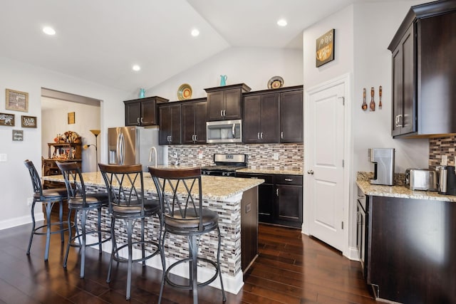 kitchen featuring appliances with stainless steel finishes, lofted ceiling, a kitchen island, a kitchen breakfast bar, and backsplash