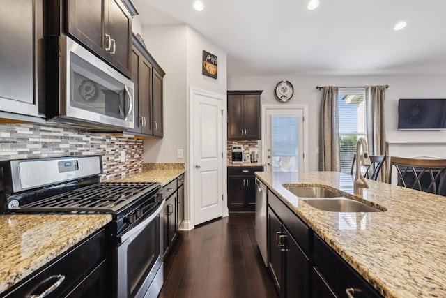 kitchen featuring appliances with stainless steel finishes, backsplash, dark brown cabinets, light stone countertops, and sink