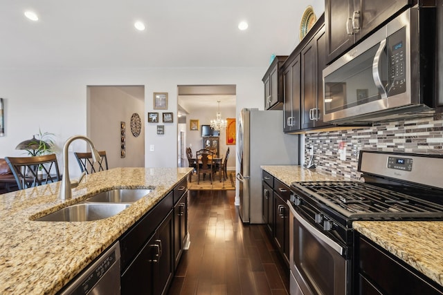 kitchen with appliances with stainless steel finishes, dark wood-type flooring, tasteful backsplash, sink, and light stone counters