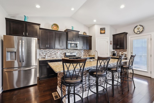 kitchen with lofted ceiling, a breakfast bar, a kitchen island with sink, appliances with stainless steel finishes, and light stone counters