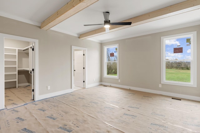 unfurnished bedroom featuring ceiling fan, multiple windows, a walk in closet, and beam ceiling