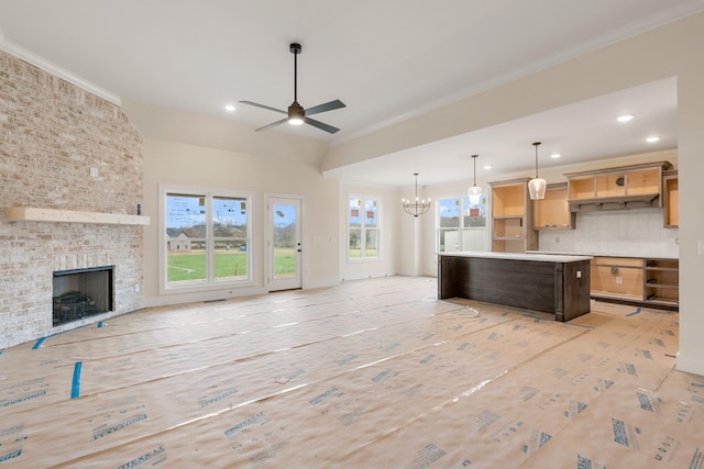 kitchen featuring ceiling fan with notable chandelier, a center island, tasteful backsplash, a brick fireplace, and crown molding