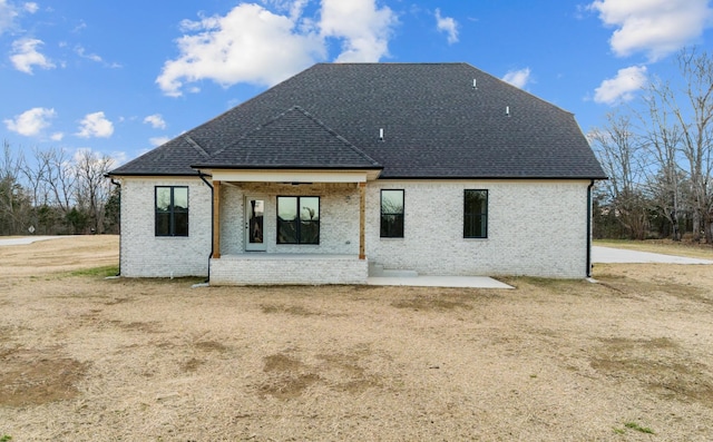 rear view of property featuring brick siding, a shingled roof, a yard, and a patio