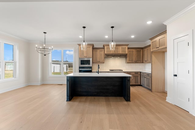 kitchen featuring an island with sink, stainless steel microwave, oven, light countertops, and pendant lighting