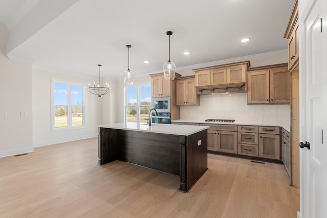 kitchen featuring a center island with sink, hanging light fixtures, built in microwave, light countertops, and stainless steel oven