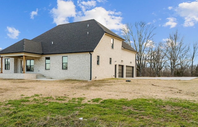 rear view of property featuring a garage, a shingled roof, and brick siding