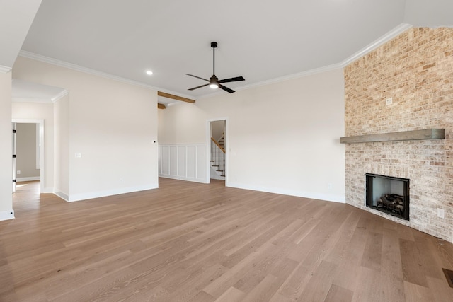 unfurnished living room featuring stairway, ornamental molding, a brick fireplace, ceiling fan, and light wood-type flooring