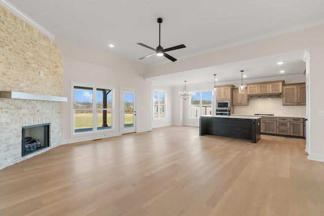 unfurnished living room with crown molding, a brick fireplace, plenty of natural light, and light wood finished floors