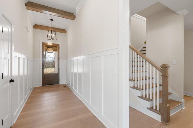 entryway featuring a wainscoted wall, light wood finished floors, beamed ceiling, and a decorative wall