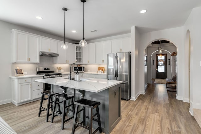 kitchen with stainless steel appliances, a kitchen island with sink, and white cabinets